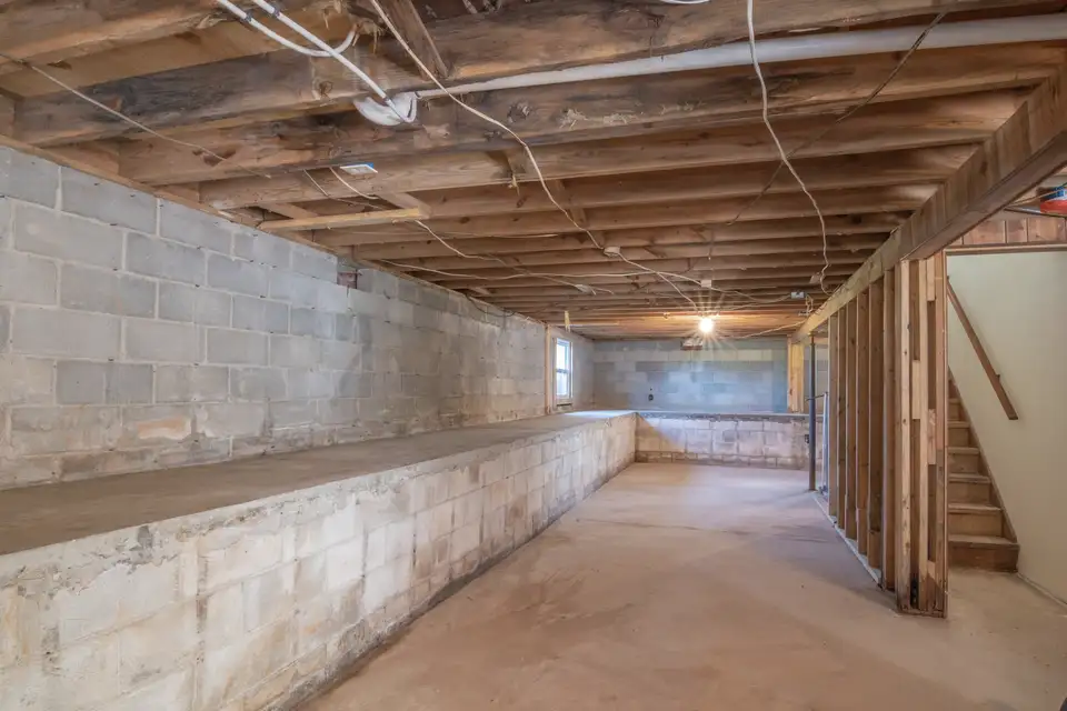 Unfinished basement with exposed joists and concrete walls