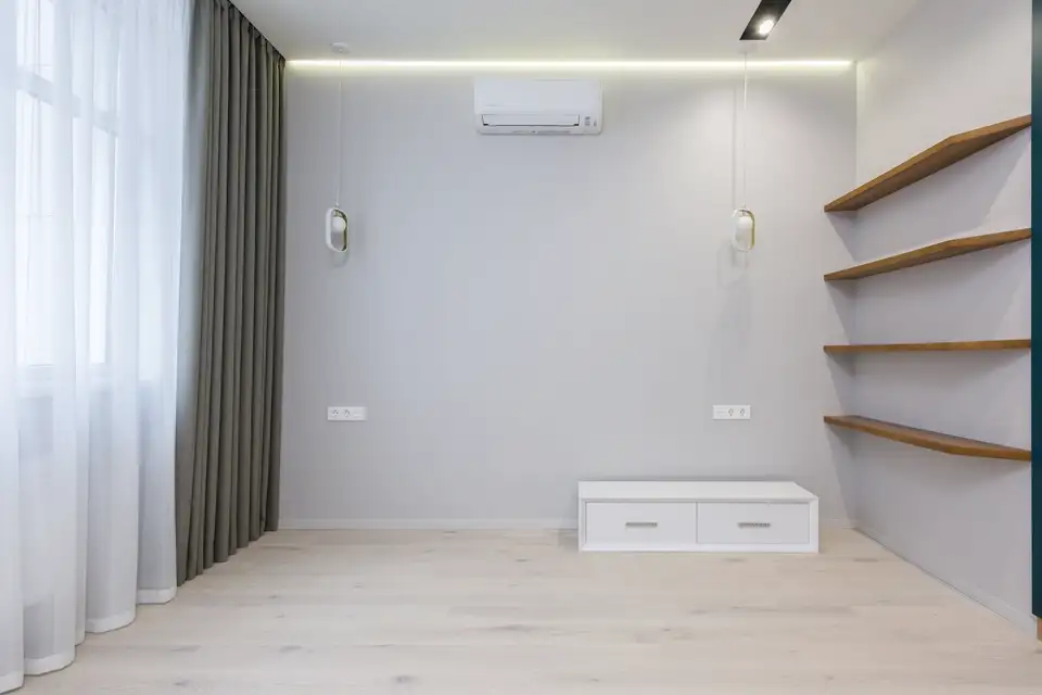 Wall-mounted ductless indoor unit high on a pale wall in an empty living room