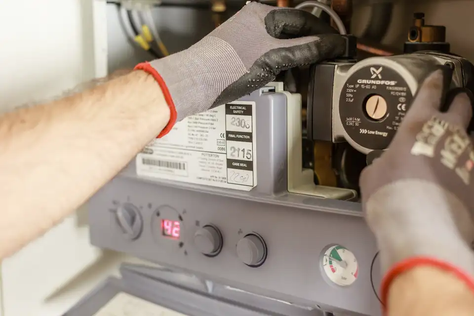 Technician's gloved hands adjusting the controls of a heating unit